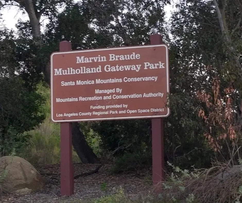 Entrance sign at Marvin Braude Mulholland Gateway Park surrounded by trees and shrubs, welcoming visitors to a scenic nature area in Tarzana, California.