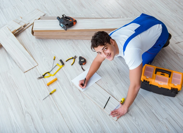 "Installer measuring and positioning vinyl flooring planks with tools spread out for a precise home flooring project."