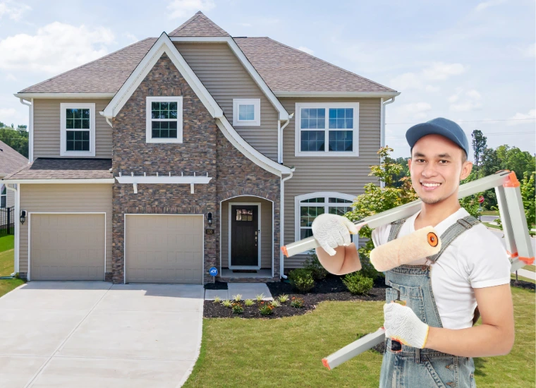Smiling professional painter holding paint rollers in front of a freshly painted two-story home with brick and siding exterior, showcasing the quality craftsmanship of O'Brien & Sons Builders.